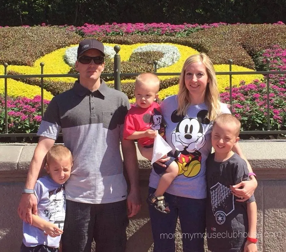 A family of 5 posed in front of a Mickey Mouse made out of flowers at Magic Kingdom.