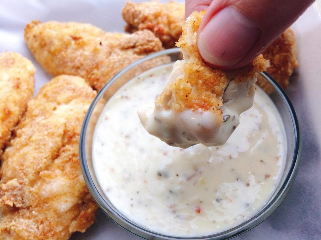 A piece of chicken being dipped into Garlic Parmesan Dipping Sauce.