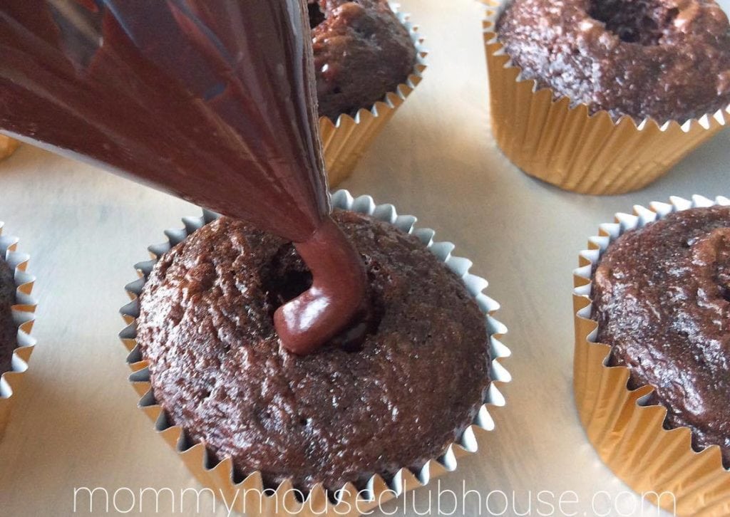 Chocolate ganache being piped into cupcakes to make Chocolate Salted Caramel Cupcakes