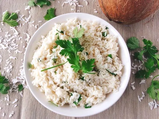 Easy Five Minute Coconut Rice in a bowl surrounded by a coconut, coconut flakes and cilantro