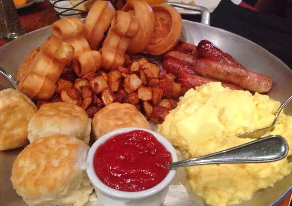 Plate full of Mickey Waffles, hash browns, bacon ,sausage, eggs, biscuits, and ketchup