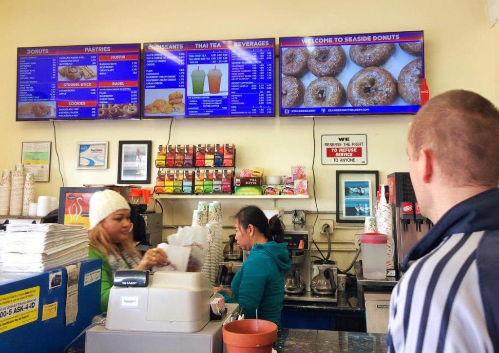 Customers in a donut shop looking at the menu.