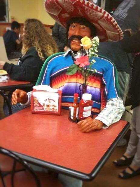 A manequin in a sombrero sitting at a table.