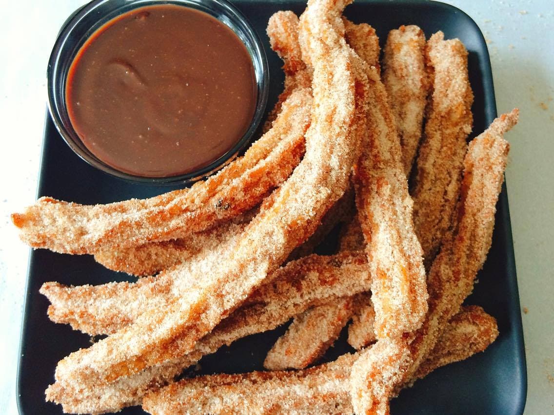 Churros on a plate with a dish of hot fudge.