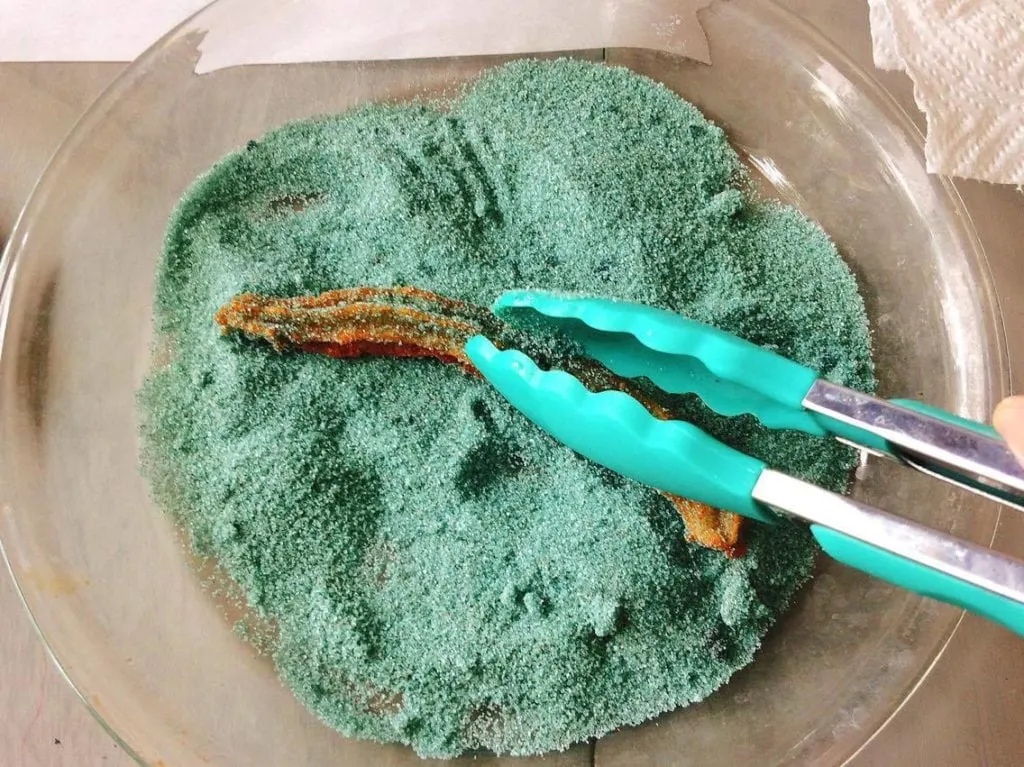 Homemade Disney Churros being dusted with blue cinnamon sugar held by blue silicone tongs.