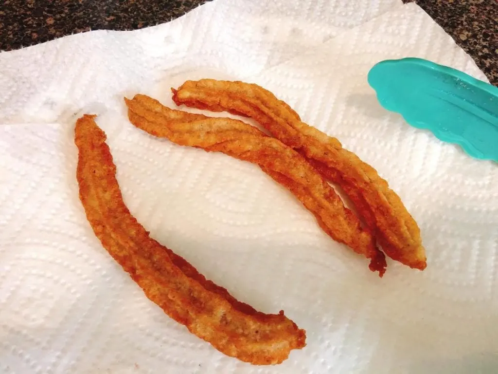 Homemade Disney Churros just removed from oil and placed on a paper towel with silicone tongs.