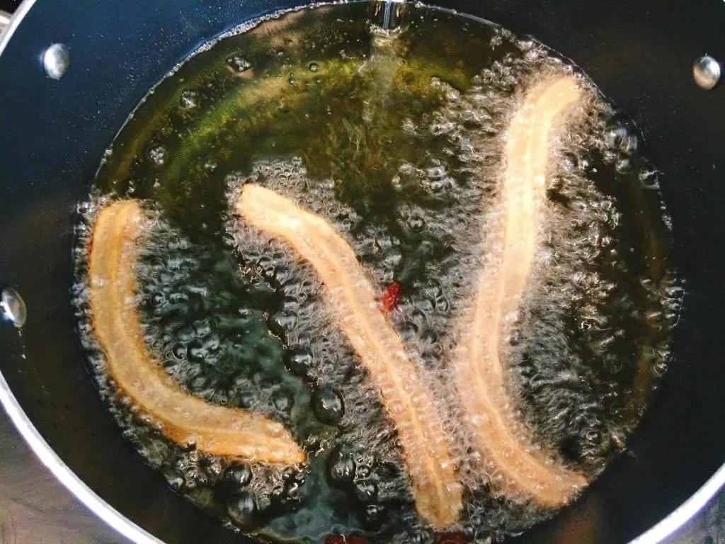 Homemade Disney Churros being fried in oil in a pan.