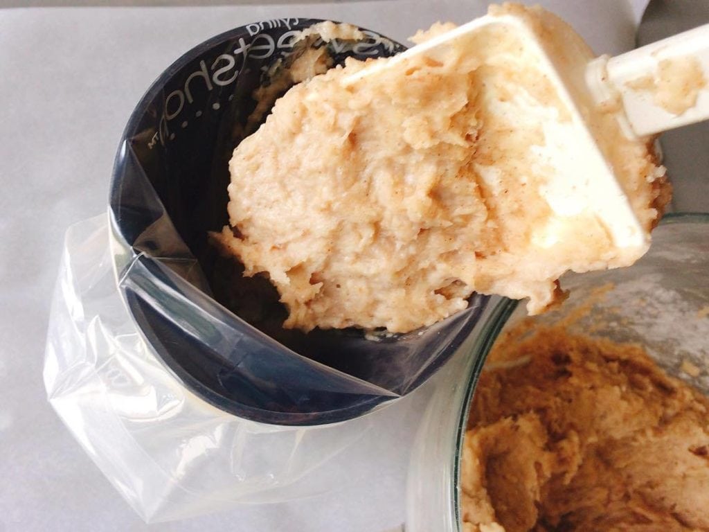 Homemade Disney Churros dough being put in a cup with a disposable piping bag.