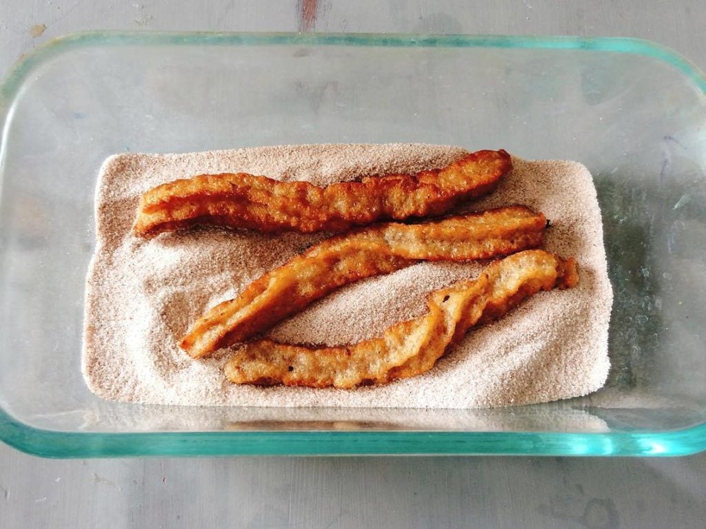 Homemade Disney Churros laying in a dish with cinnamon sugar.