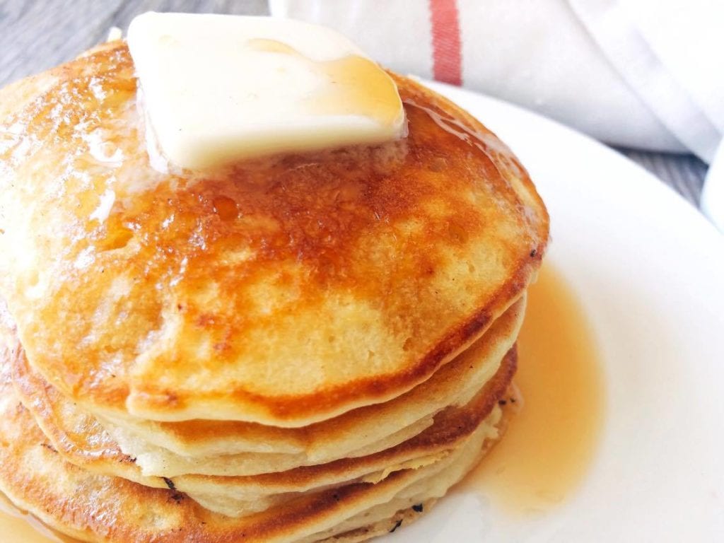 Stack of sweet cream pancakes topped with butter and syrup.