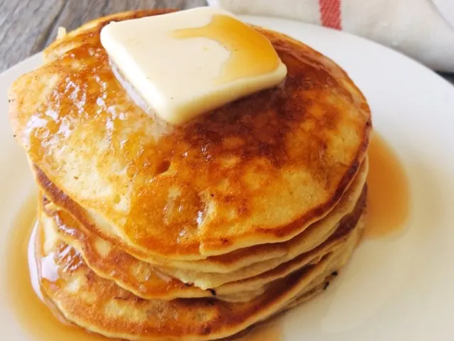 Pancakes on a white plate topped with butter and syrup.