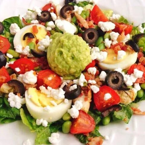 A copycat Zupas California Protein Cobb Salad with lettuce, tomatoes, olives, hard boiled eggs, avocado, and feta cheese.