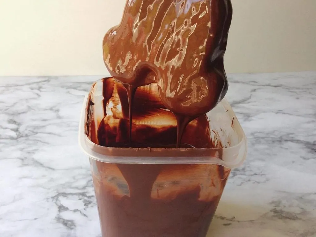 A Mickey Mouse shaped ice cream bar just dipped in chocolate over a container of chocolate to make Homemade Hand Dipped Ice Cream Bars