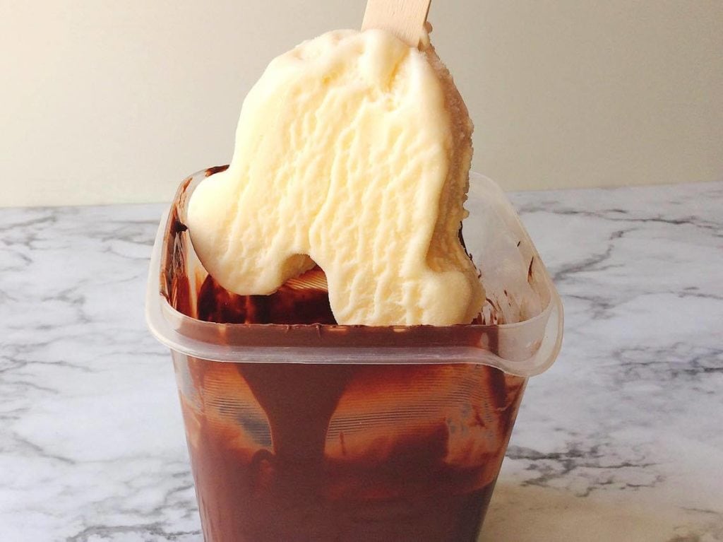 A vanilla Mickey Mouse shaped ice cream bar being dipped in chocolate to make Homemade Hand Dipped Ice Cream Bars