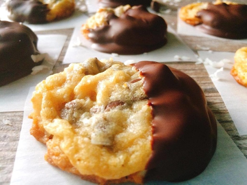 Almond Joy Chocolate Chip Cookies dipped in chocolate on parchment paper squares.