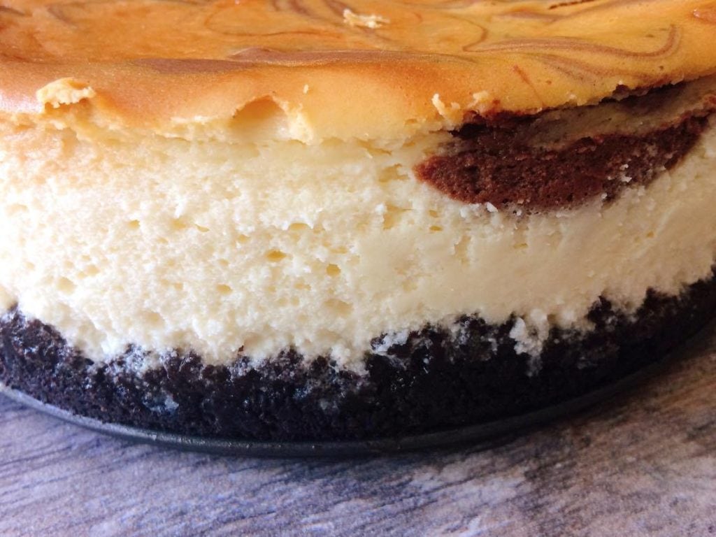 A side view of Caramel Pecan Turtle Cheesecake, a cookie crust and classic cheesecake swirled with chocolate cheesecake.