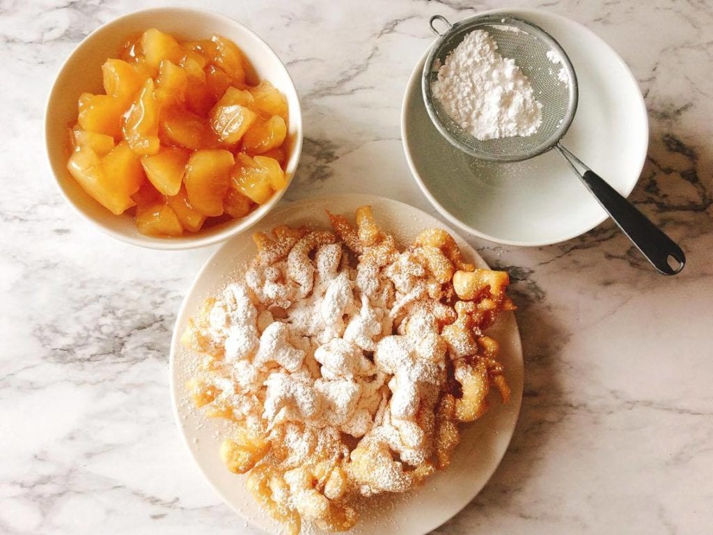 Apple pie filling in a bowl, powdered sugar in a bowl and a funnel cake on a plate, shaped like a Mickey Mouse head just like Disneyland's Apple Pie Funnel Cake