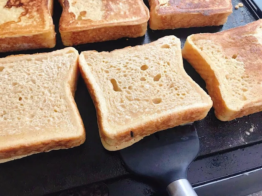 A slice of French Toast ready to be flipped over by a spatula