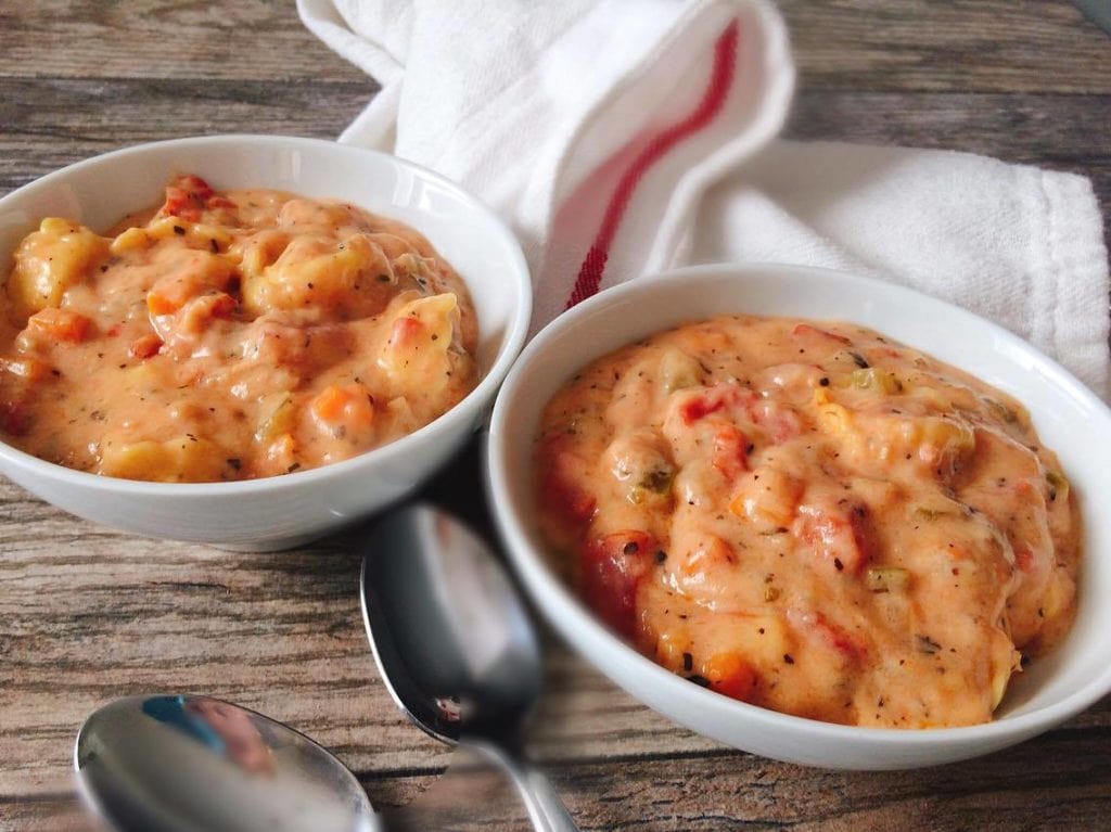 Two bows of Instant Pot Cheesy Tortellini Tomato Soup, two spoons, and a kitchen towel.