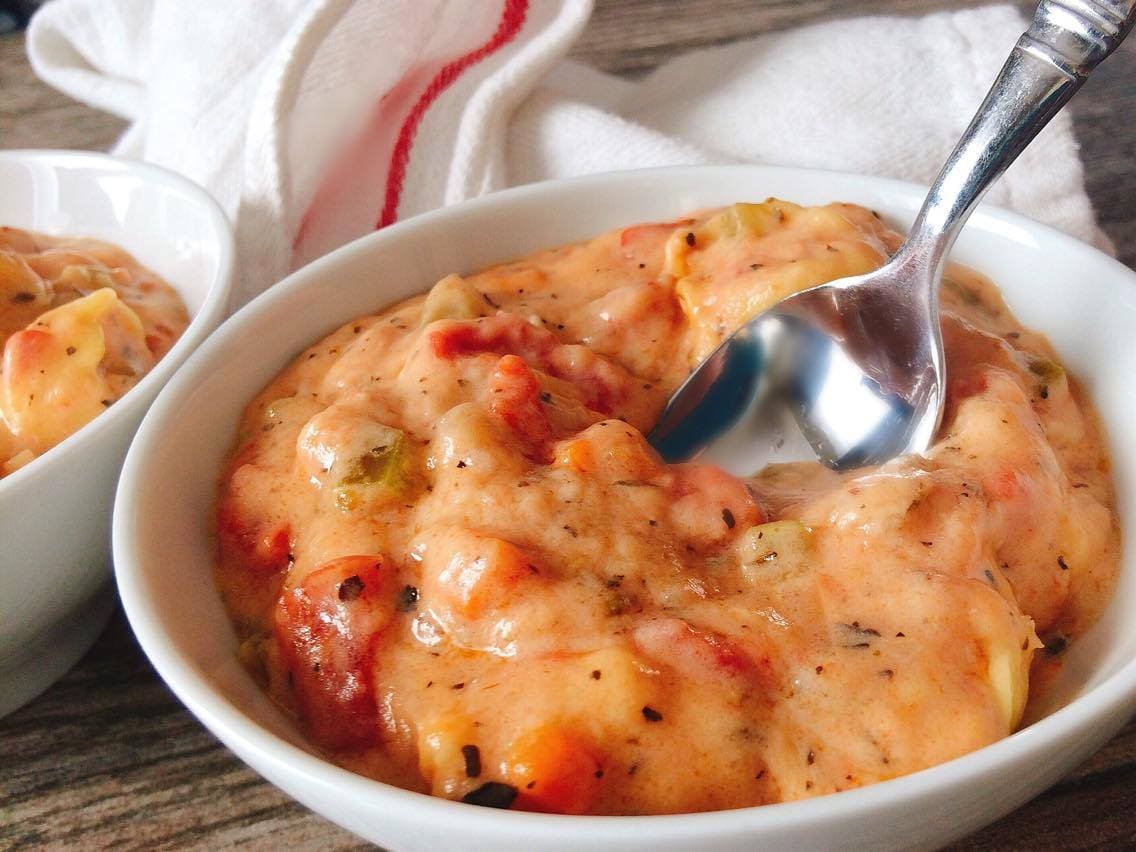 A bowl of cheesy tortellini tomato soup with a spoon