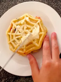 A child's hands spreading butter on a waffle to make Grilled Sweet Berry Waffle Sandwich