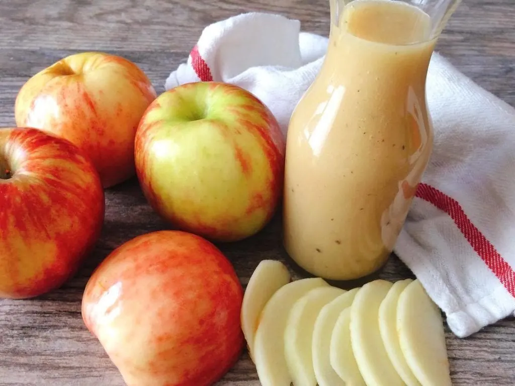 A jar of salad dressing surrounded by apples and a kitchen towel to make Honeycrisp Harvest Salad