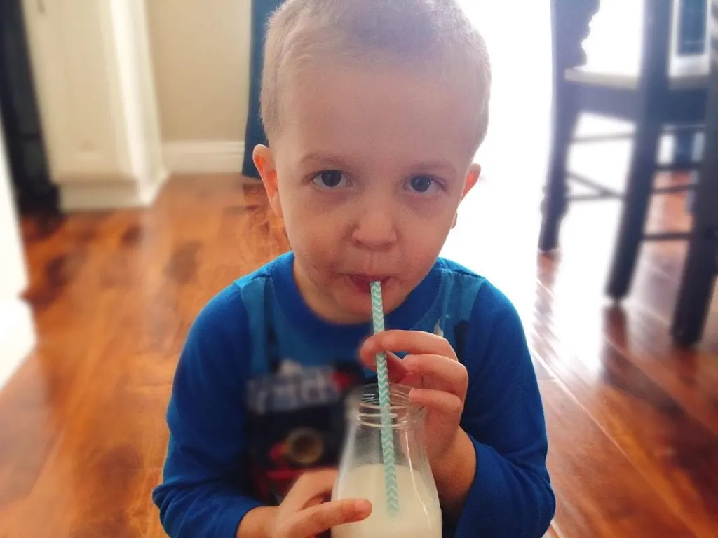 A little boy drinking milk from a bottle with a straw