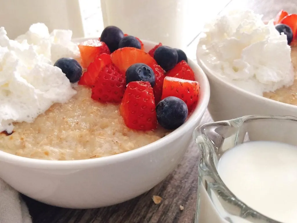 Two bowls of Creamy Half Baked Oatmeal made with Milk with whipped cream and berries