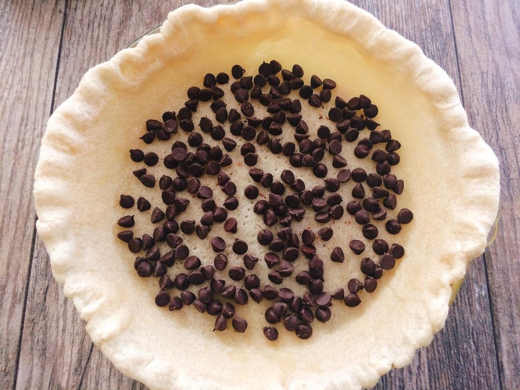 Chocolate chips sprinkled over a pie crust to make Dark Chocolate Pecan Pie