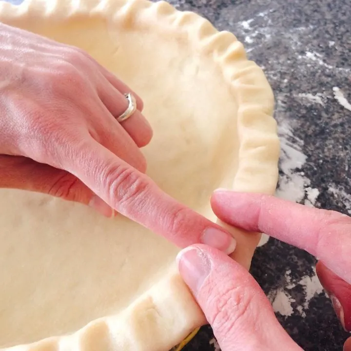 Two hands shaping a Flaky All=Butter Pie Crust in a pie pan.