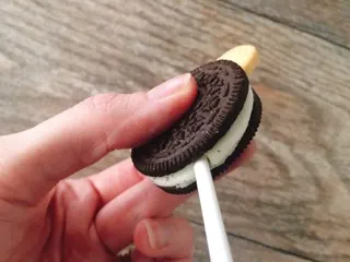 A hand holding an Oreo with a stick.