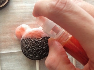 A hand spraying edible glitter on an Oreo.