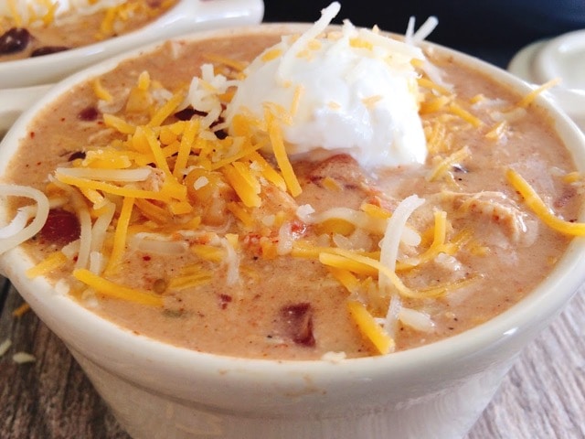 A bowl of creamy chicken chili topped with cheese and sour cream.