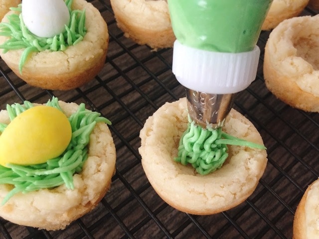 Green frosting being.piped into a sugar cookie cup