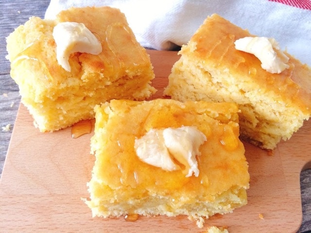 Three pieces of cornbread topped with butter an honey.