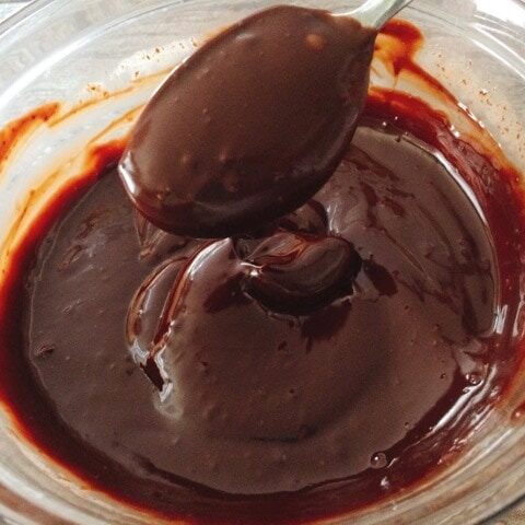 A spoonful of chocolate ganache over a bowl of melted chocolate.