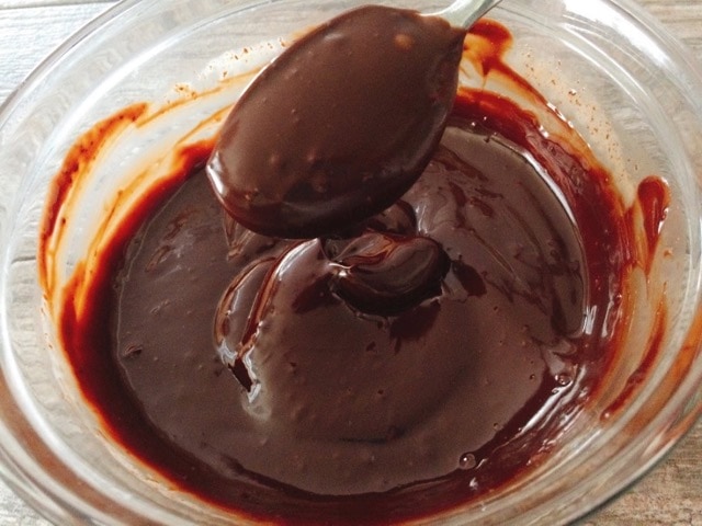 A spoonful of chocolate ganache over a bowl of melted chocolate.