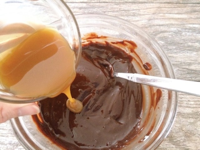 A dish of caramel being poured into melted chocolate.