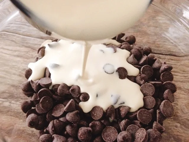 Heavy cream being poured over chocolate chips.