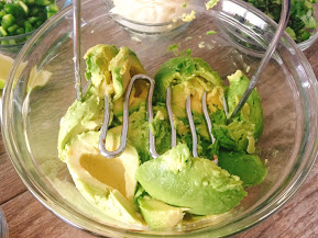 A bowl of avocados being smashed by a potato masher.