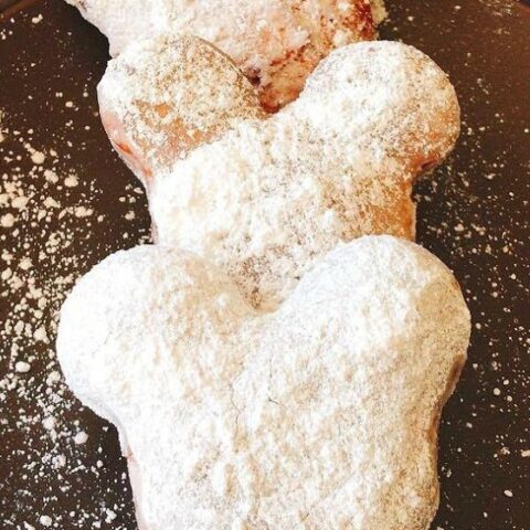 Three homemade Mickey Mouse shaped beignets covered in powdered sugar