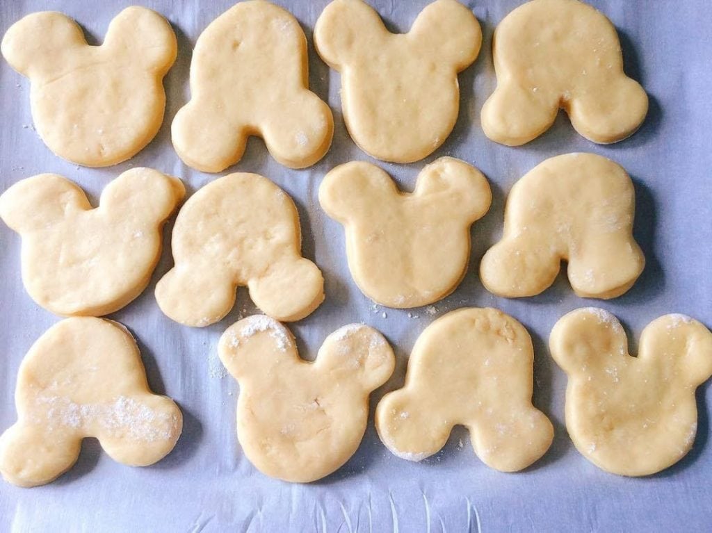 Beignet dough shaped like Mickey Mouse on a baking sheet.
