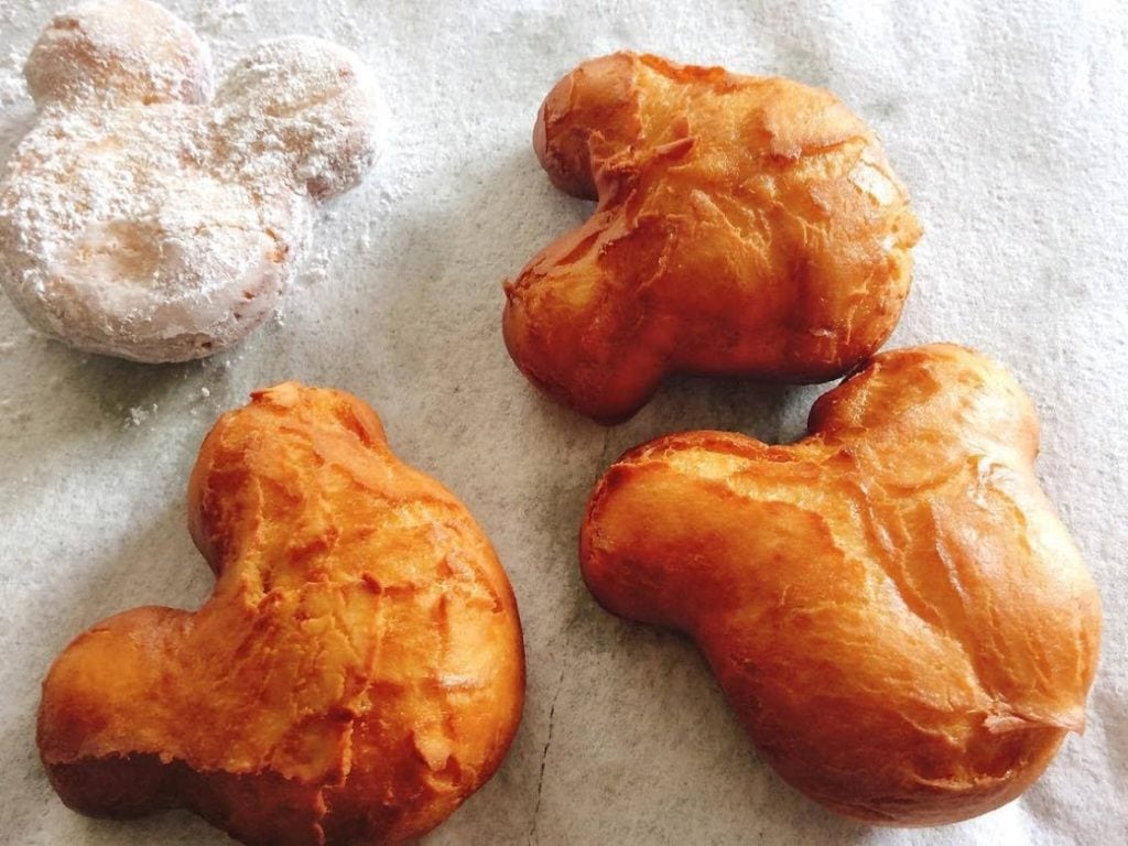 Three plain Mickey shaped beignets plus one beignet covered in powdered sugar.