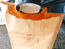 Powdered Sugar in a measuring cup being poured into a paper sack.