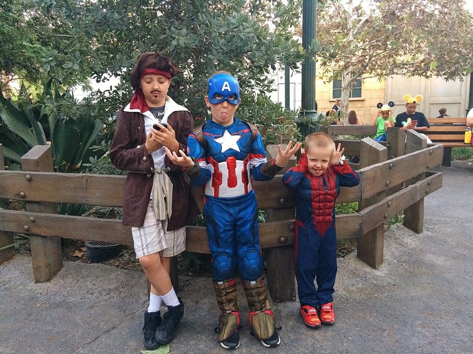 Three boys dressed in costumes in front of a fence.