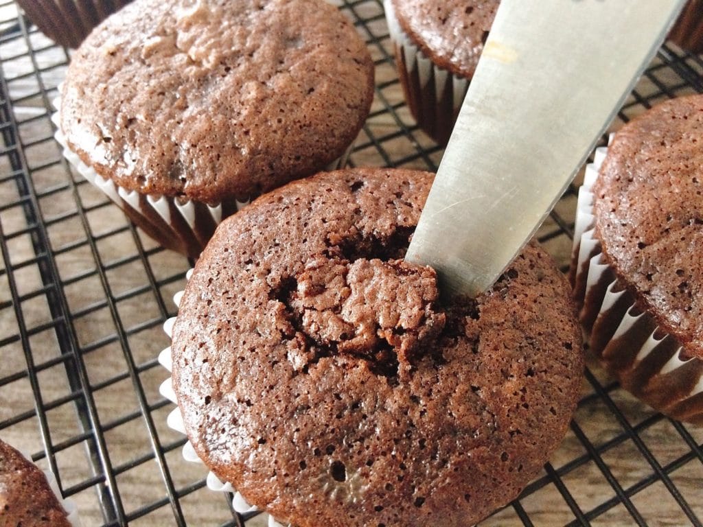 A knife cutting the center out of a chocolate cupcake. Step 2.