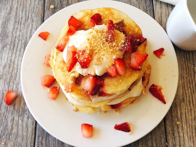 A stack of Strawberry Cheesecake Pancakes sprinkled with chopped strawberries on a white plate.
