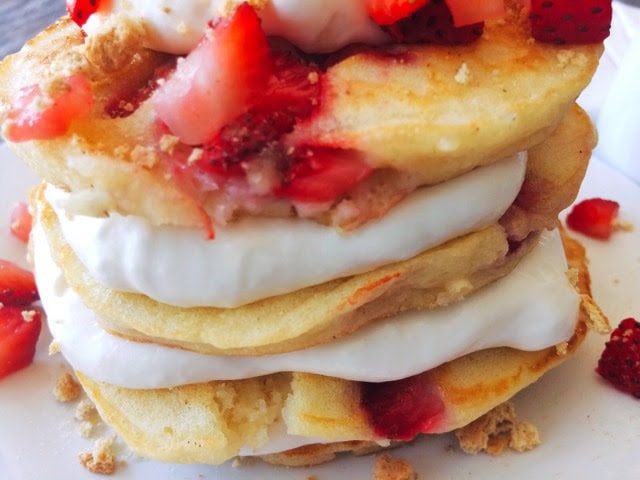 A stack Strawberry Cheesecake sprinkled with chopped strawberries and layered with Cheesecake Topping on a white plate.