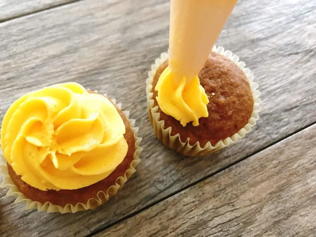 Yellow frosting being piped onto a cupcake to make Halloween Cupcakes.