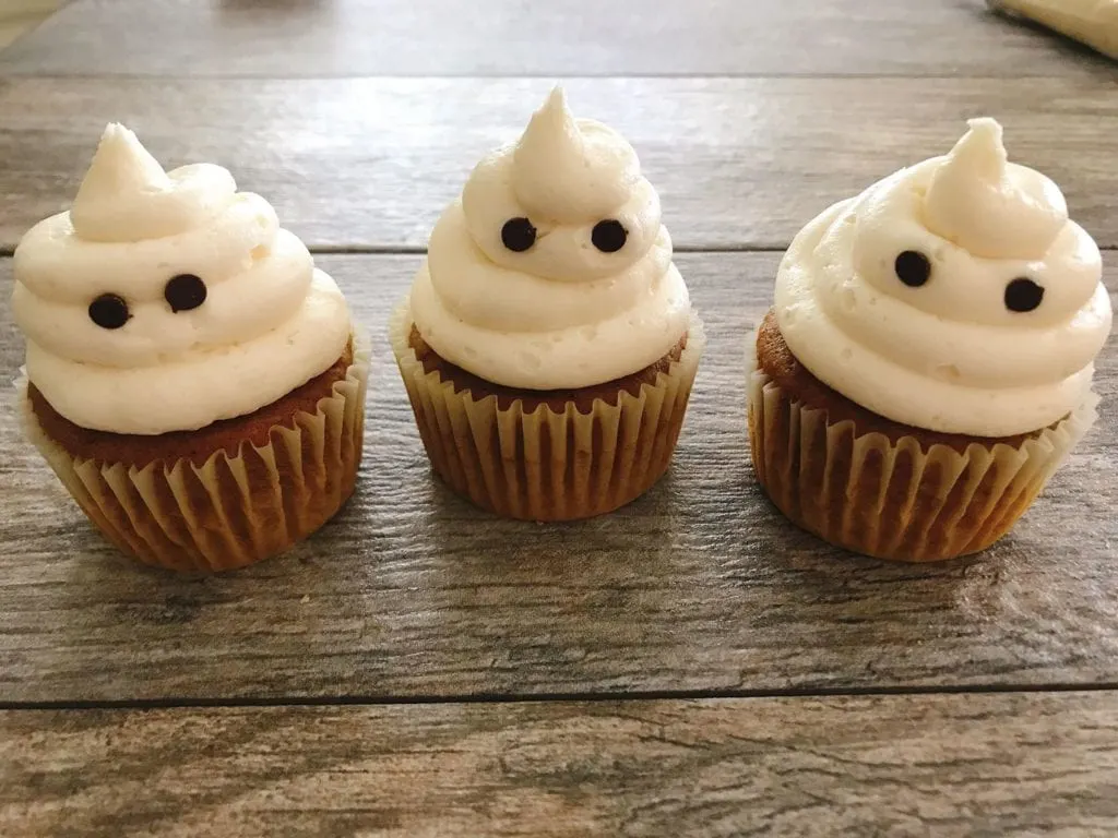 Mini chocolate chips on white frosted cupcakes to look like eyes to make Halloween Cupcakes.